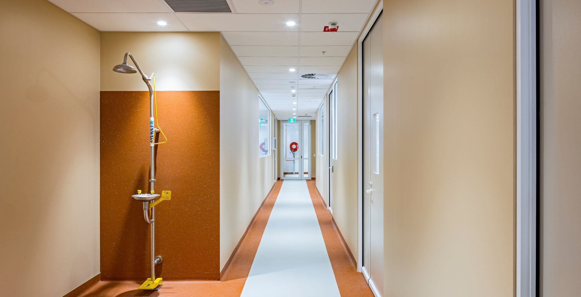 Laboratory corridor with a wall-mounted safety shower and eyewash station beside glass entry doors