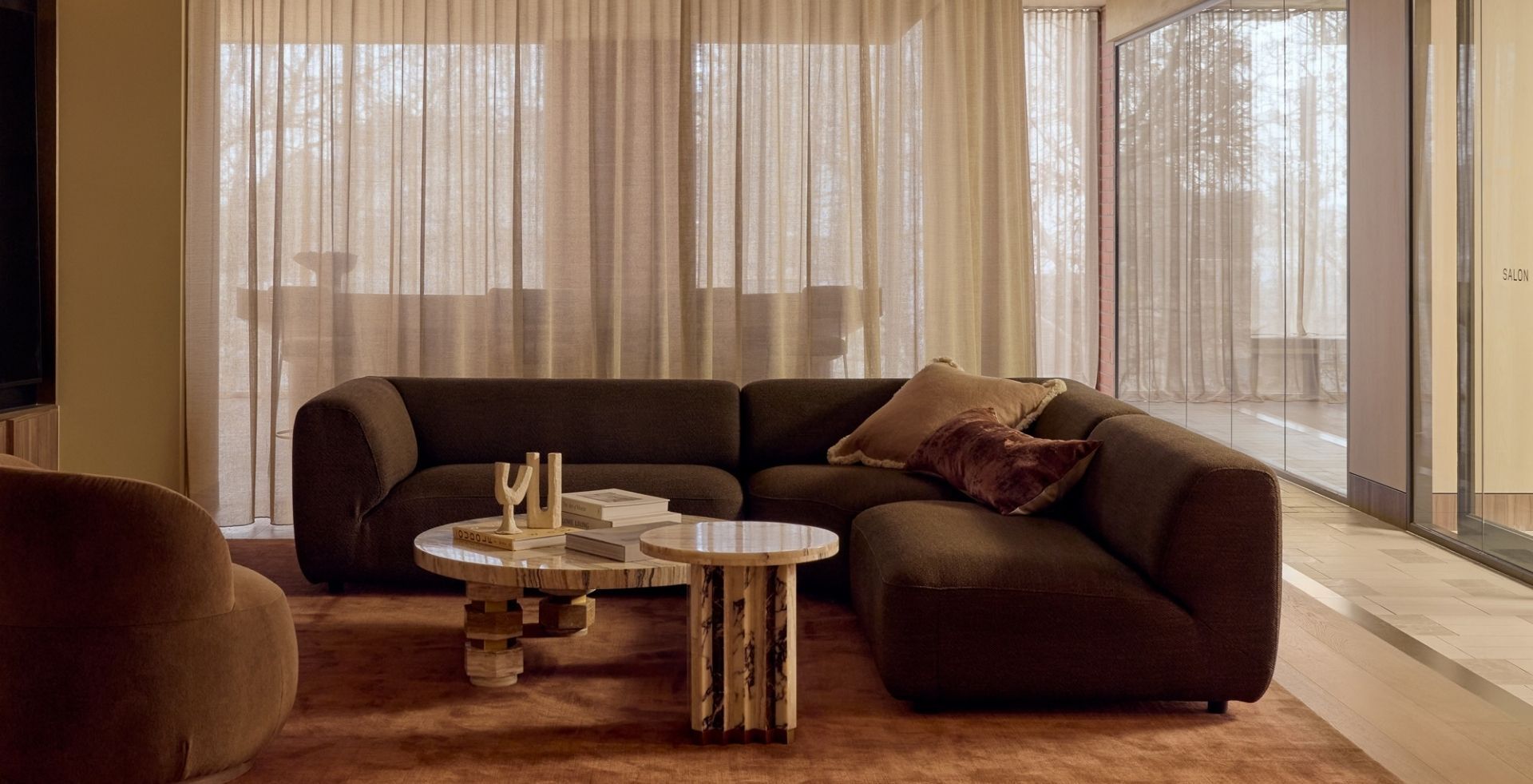 Lounge in Lowe Living's South Melbourne HQ with a dark modular sofa, stone coffee tables and sheer curtains