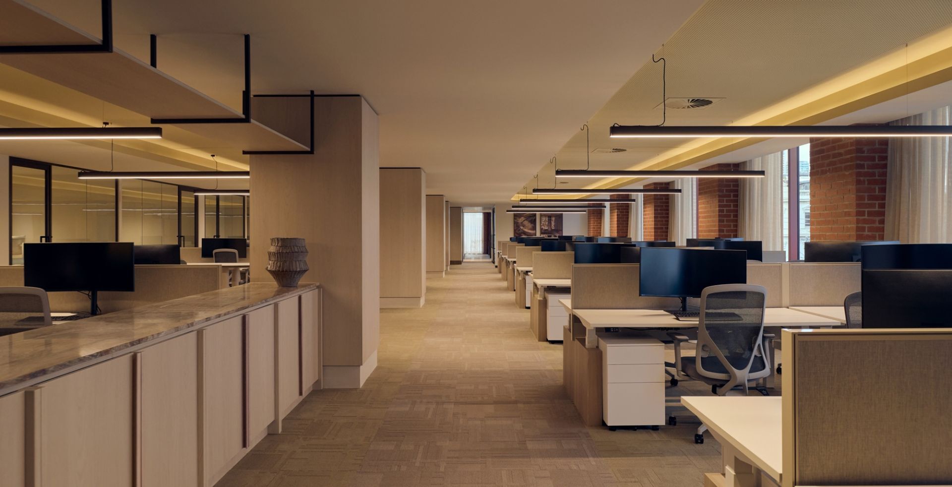 Open-plan workspace with warm linear lighting and brick columns at Lowe Living's South Melbourne office