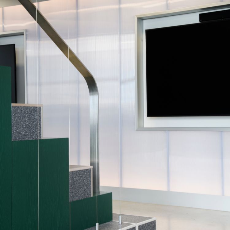 Tiered seating steps with green panels and stainless steel handrail in a modern office space.