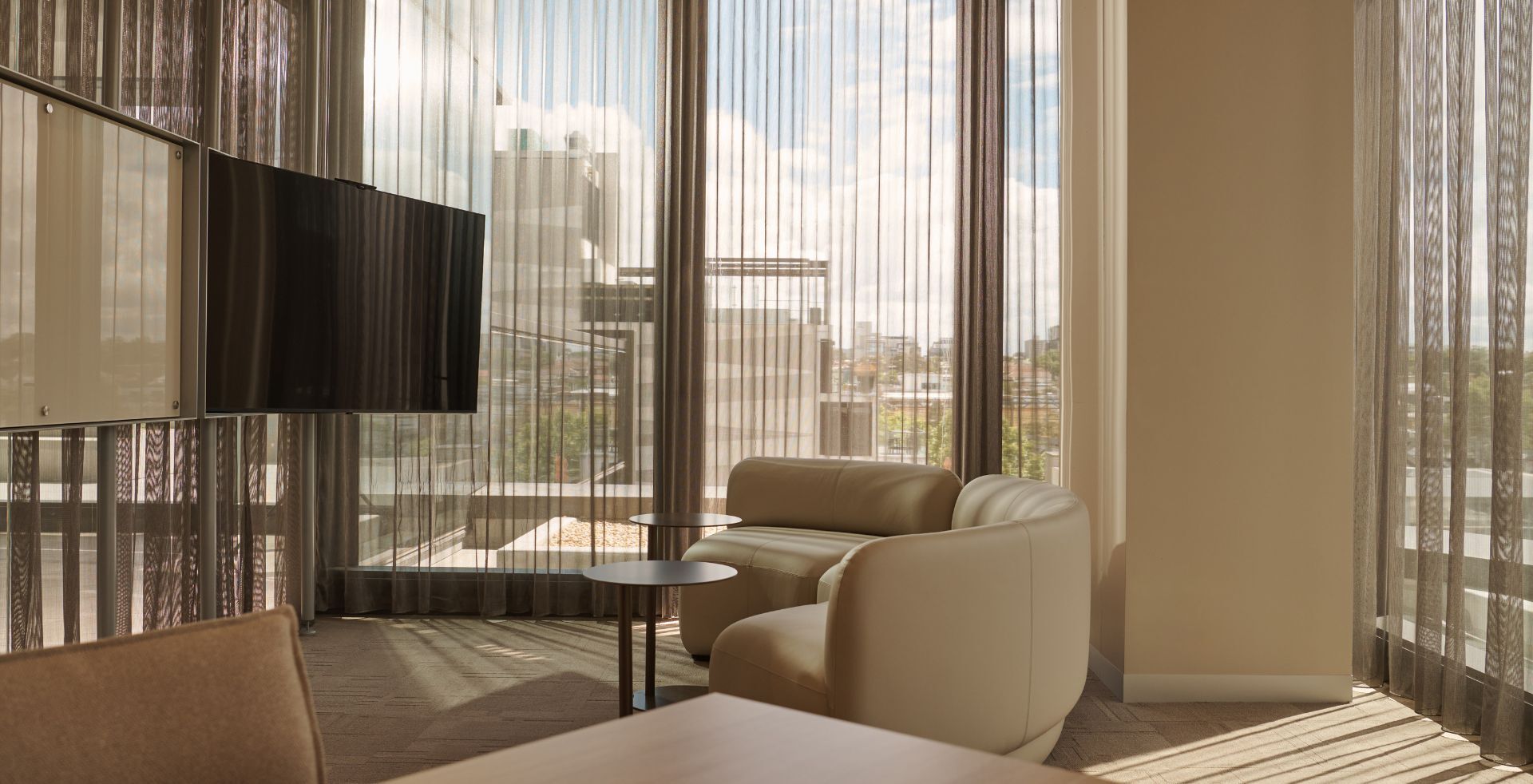 Workplace lounge with curved upholstered seating, sheer curtains and natural light overlooking the city.