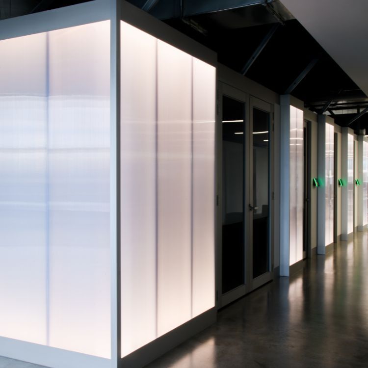 Illuminated wall panels lining a modern office corridor with glass meeting room doors.