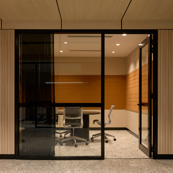 Modern meeting room with a round table and office chairs is seen through a black-framed glass partition wall at Kyko spec suite