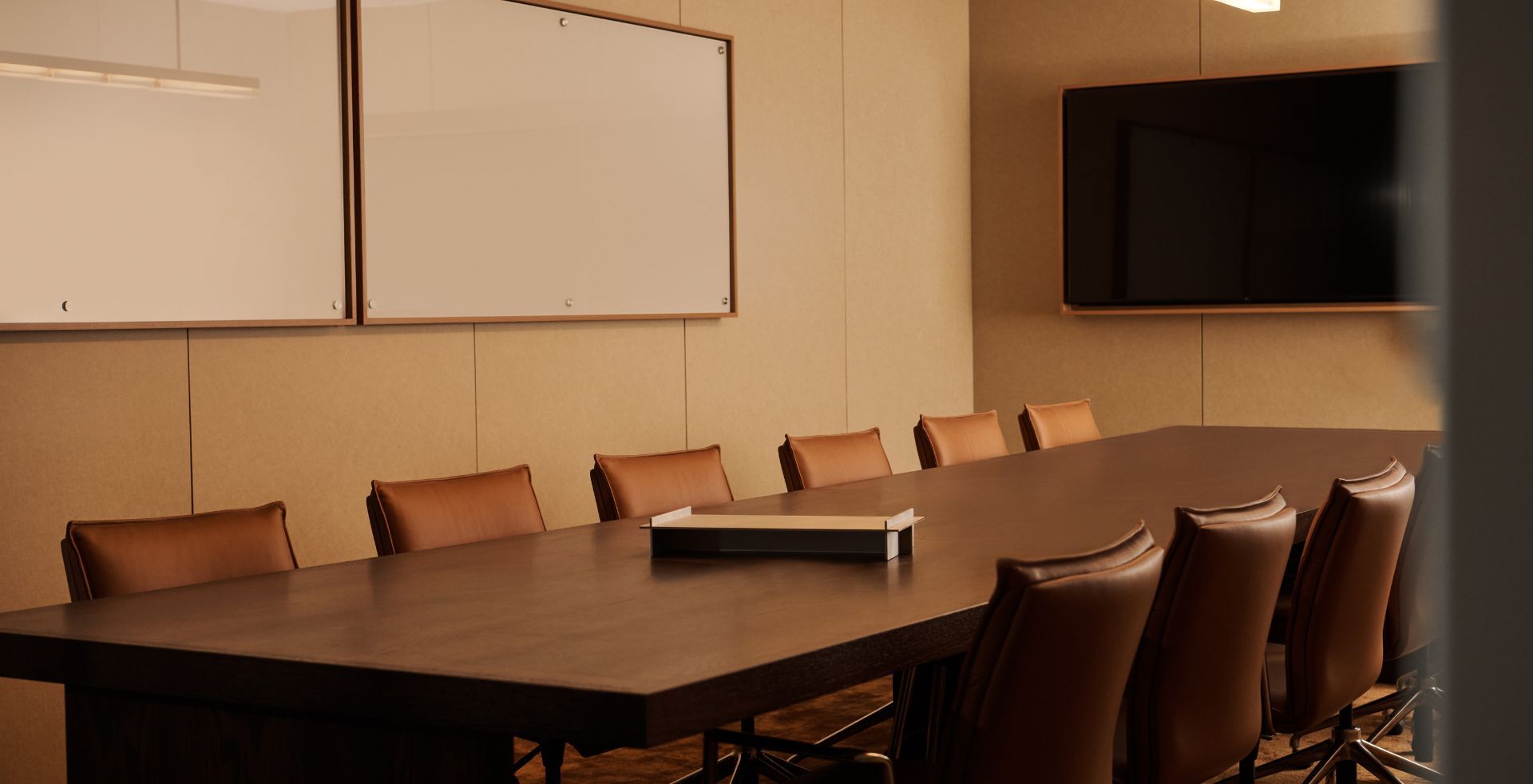 Modern boardroom with a large timber meeting table, leather chairs, acoustic wall panels and integrated lighting.