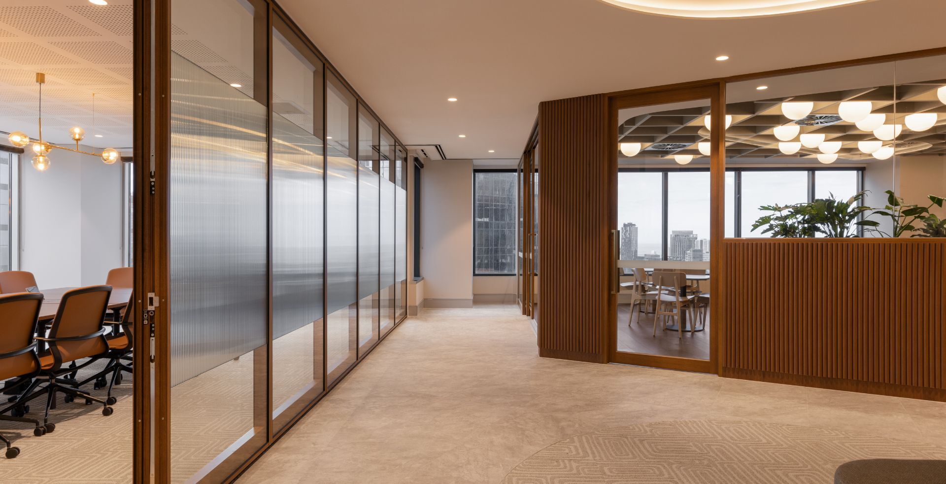 Connecting space lined with glass-fronted meeting rooms and timber joinery, leading to a breakout area