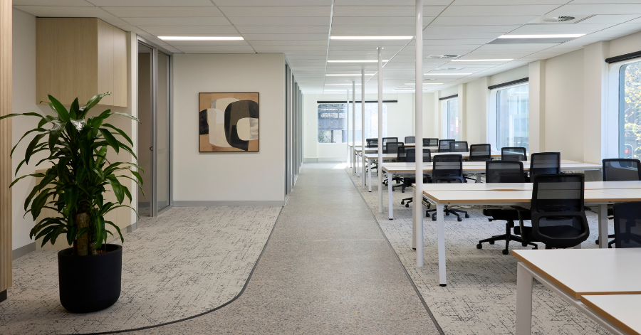 A bright, open-plan workspace within the Kyko Spec Suite features a central walkway separating rows of white desks with black mesh chairs from private office entries.