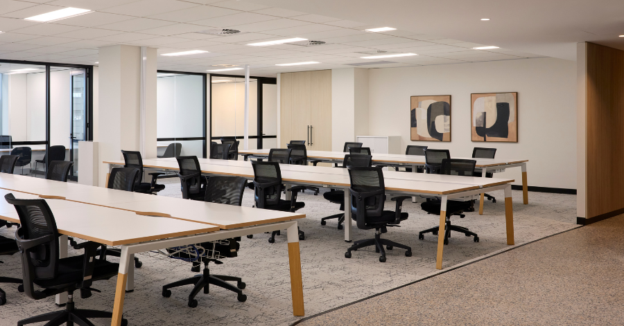 A modern open-plan workspace inside the Kyko Spec Suite features neat rows of white desks paired with black mesh office chairs on textured carpeting.