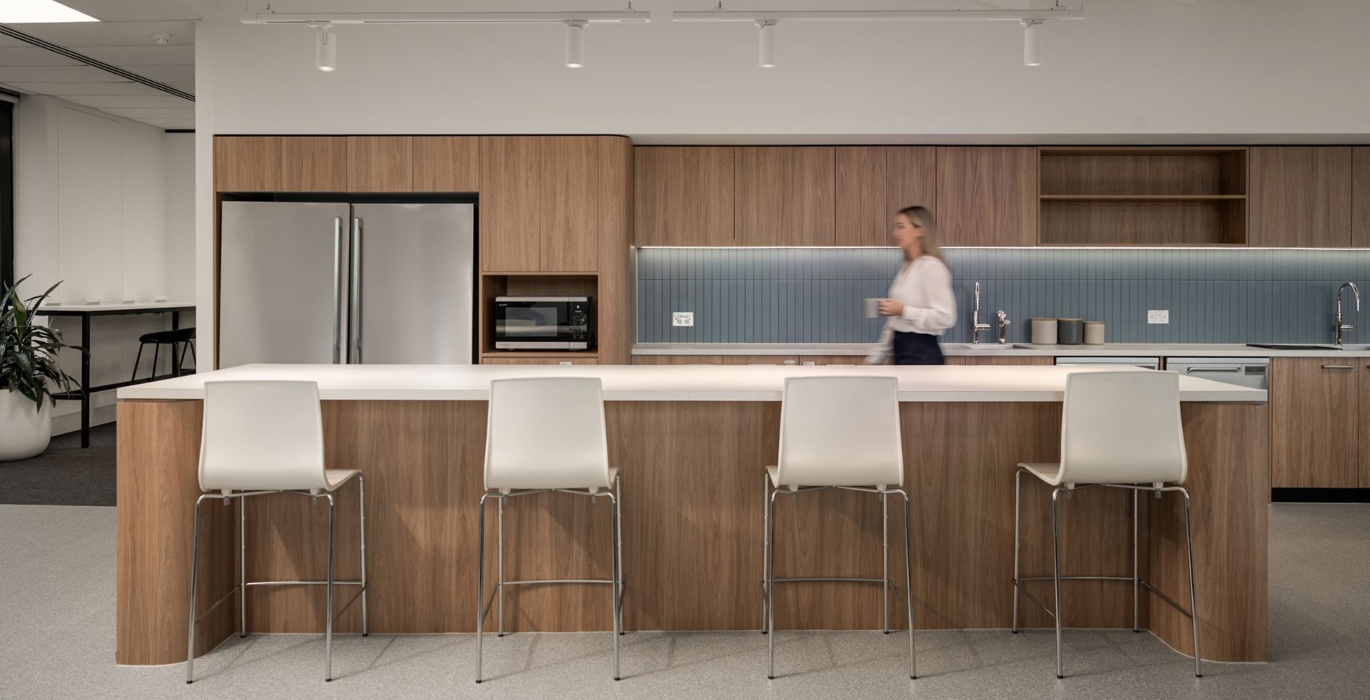 Close-up of a long timber kitchen island with white bar stools and integrated stainless steel appliances