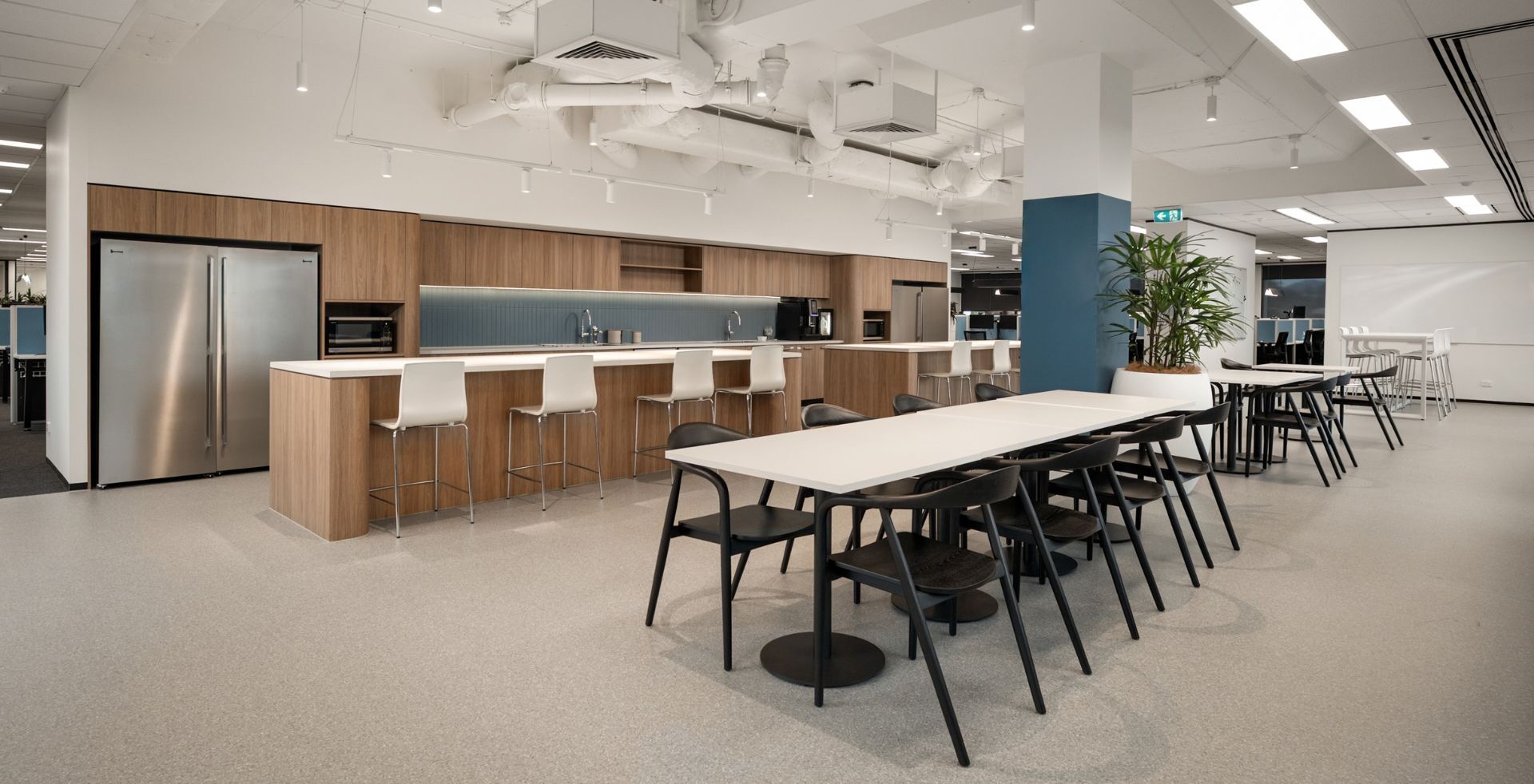 Wide view of the staff breakout cafe with a long dining table, black chairs, and timber kitchen island