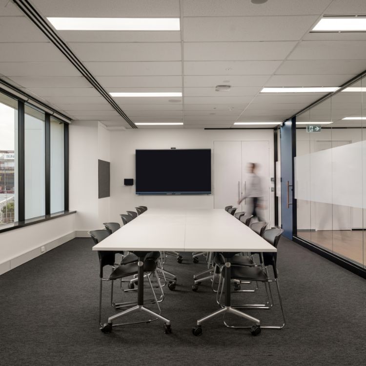 Boardroom with a long white table, black rolling chairs, large windows, and a frosted glass wall partition
