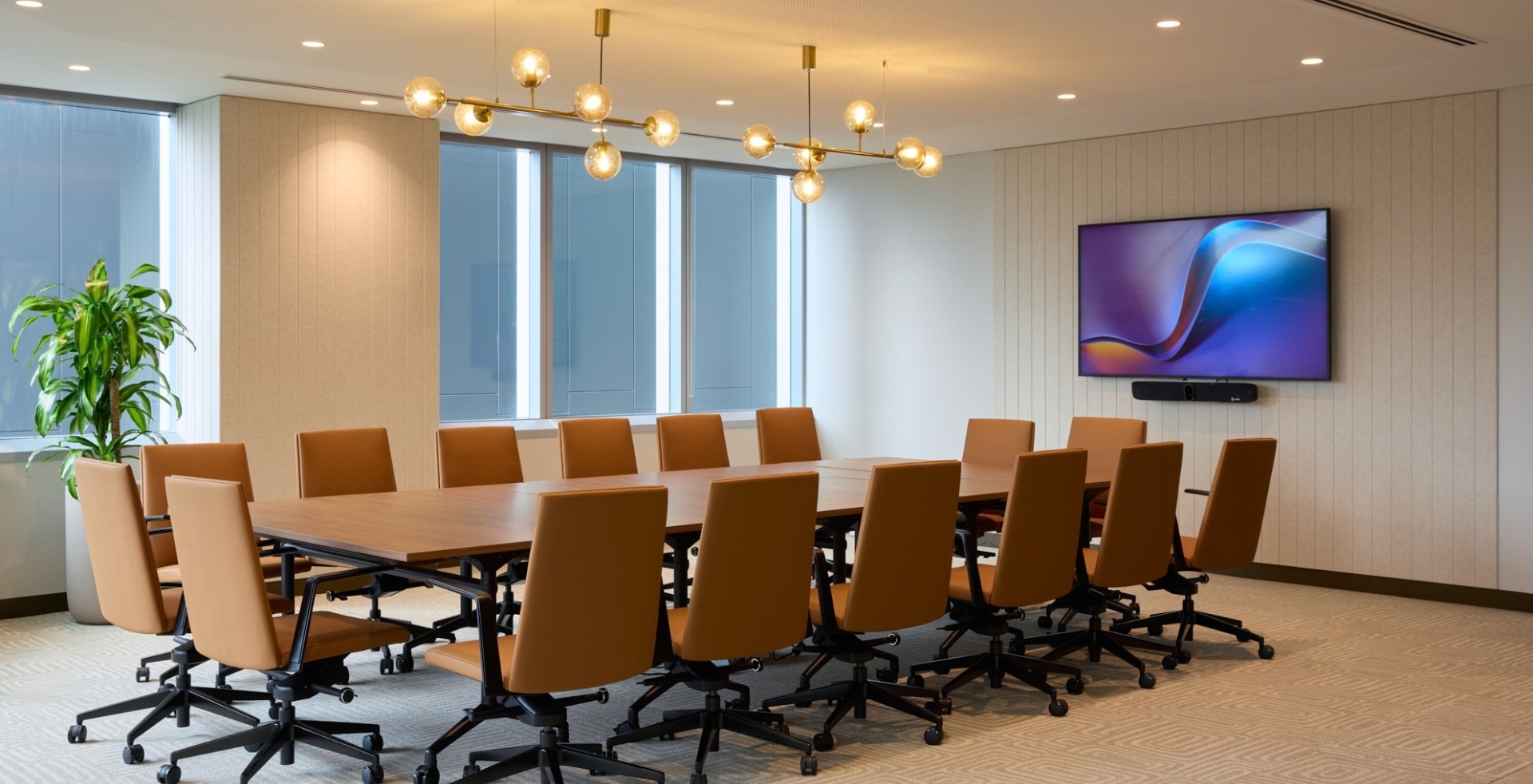 Large corporate boardroom featuring a long timber conference table, tan leather chairs, and architectural statement lighting.