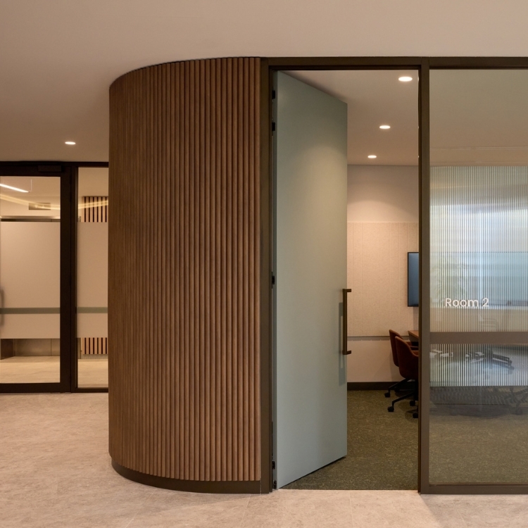Curved timber-batten feature wall and glass-fronted meeting room with a pivot door in Gilchrist Connell’s office.