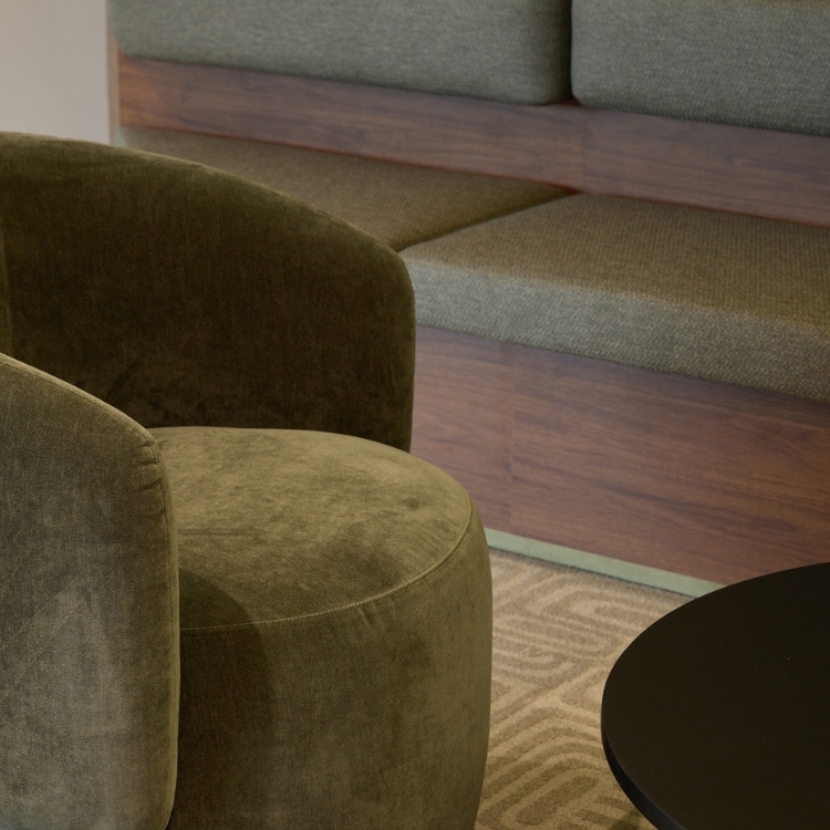 Close-up detail of a moss-green velvet armchair beside an upholstered timber bench seat in Gilchrist Connell's reception area.