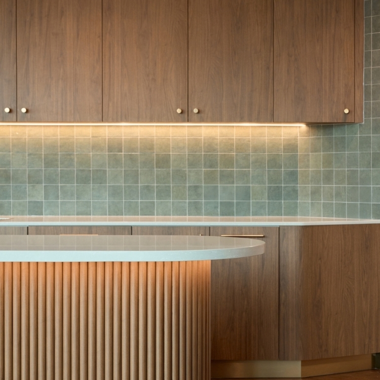 Close-up detail of a kitchen island with vertical timber-batten molding below a matching timber cabinet and green tiled backsplash.