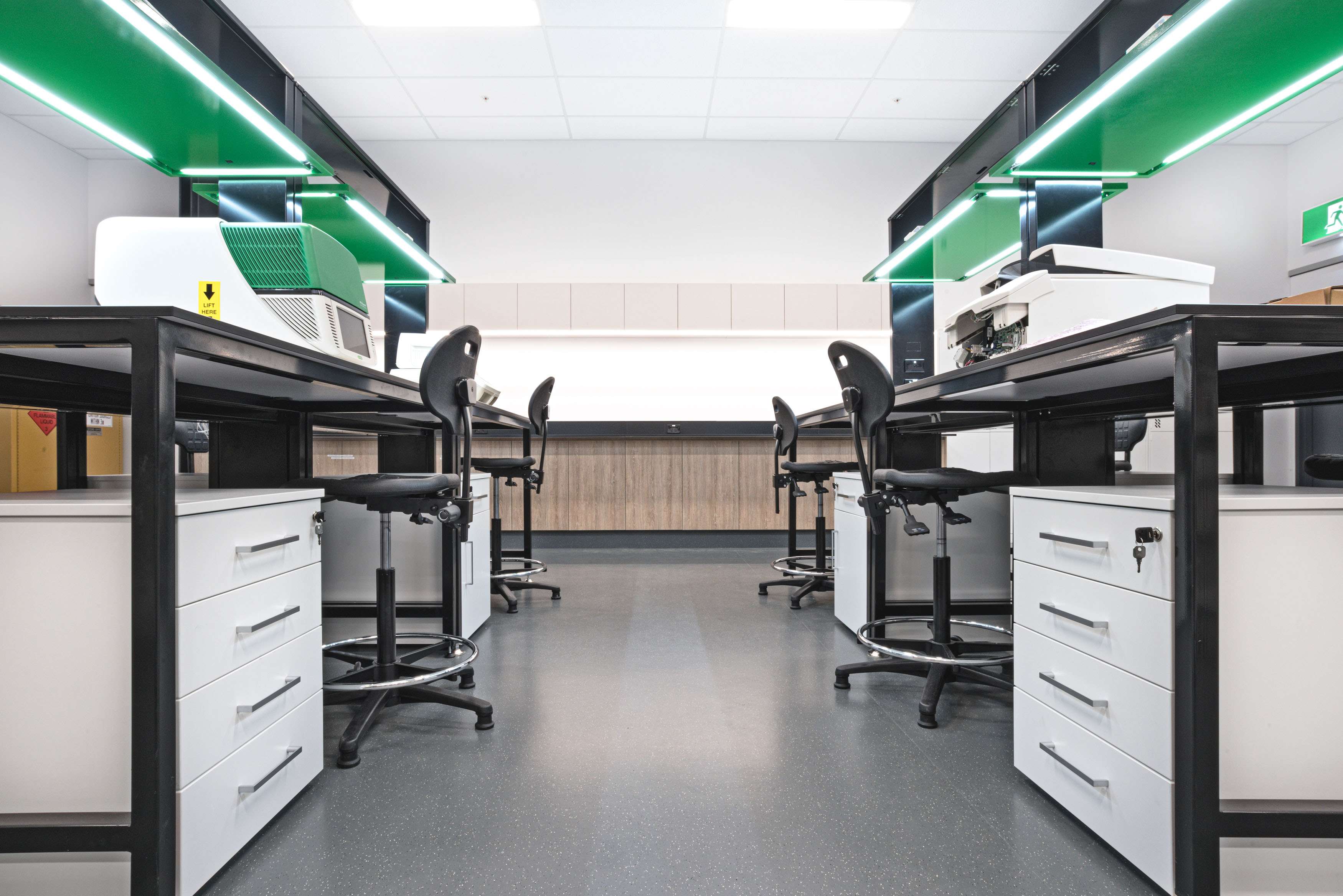 Two large desks with four chairs and plenty of storage furniture, as well as laboratory machines and shelves with light strips on them. 