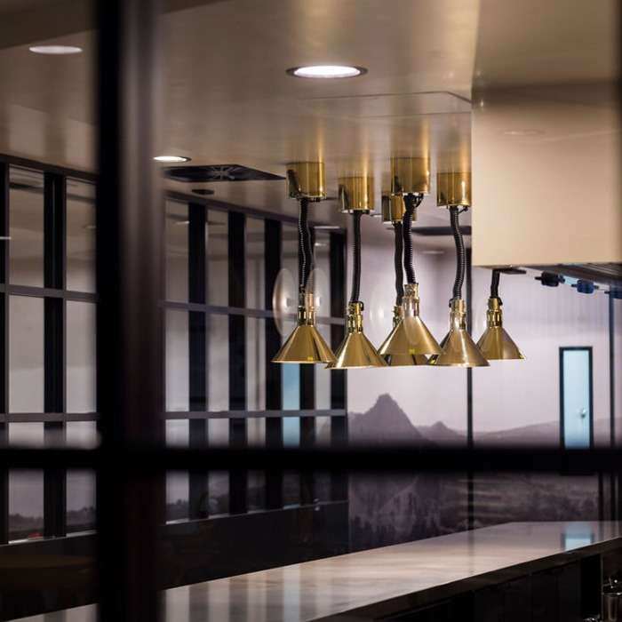 Golden heat lamps above textured marble bench top showcased in Kilcoy Global Food's employee kitchen.