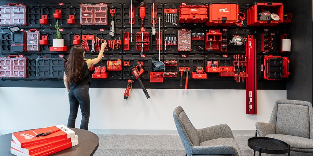 A woman stands confidently in front of a wall adorned with various tools.