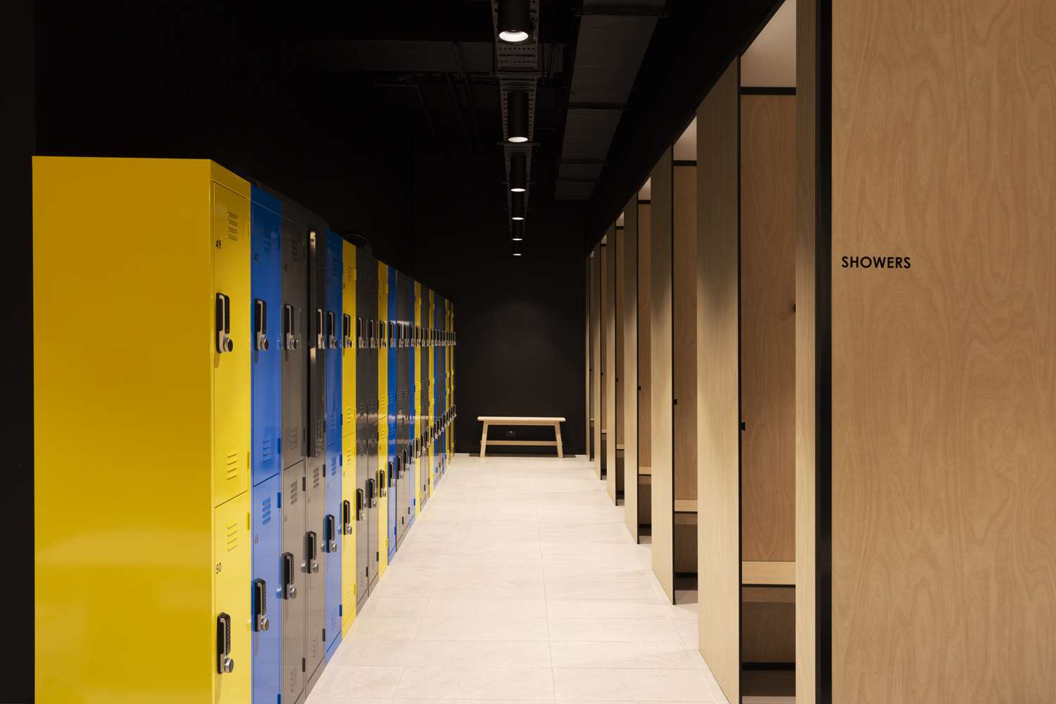 Colourful lockers on the left of the hallway and wooden cubicles on the right with the word 'SHOWERS' printed at the entrance to the room.