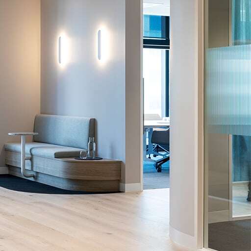 Cozy seating area with a built-in bench, small round table, and wall-mounted lights, near an office entrance.