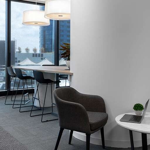 Modern office lounge with high-top chairs, a bar table, and large windows offering a view of city buildings.