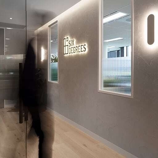 Six-Degrees-4Person walking past a glass door into an office space with a sign that reads 