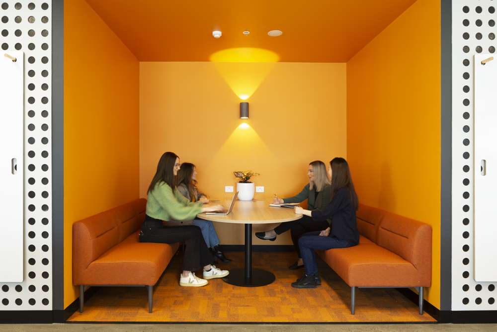 Four women meeting in bright orange meeting booth.
